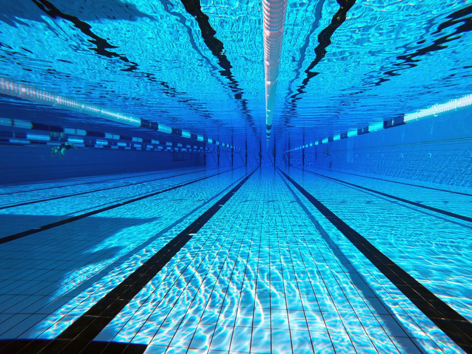 Underwater view of a well-maintained swimming pool, showcasing clear blue water, lane markers, and tiled floor, relevant to aquatic facility safety and emergency protocols.