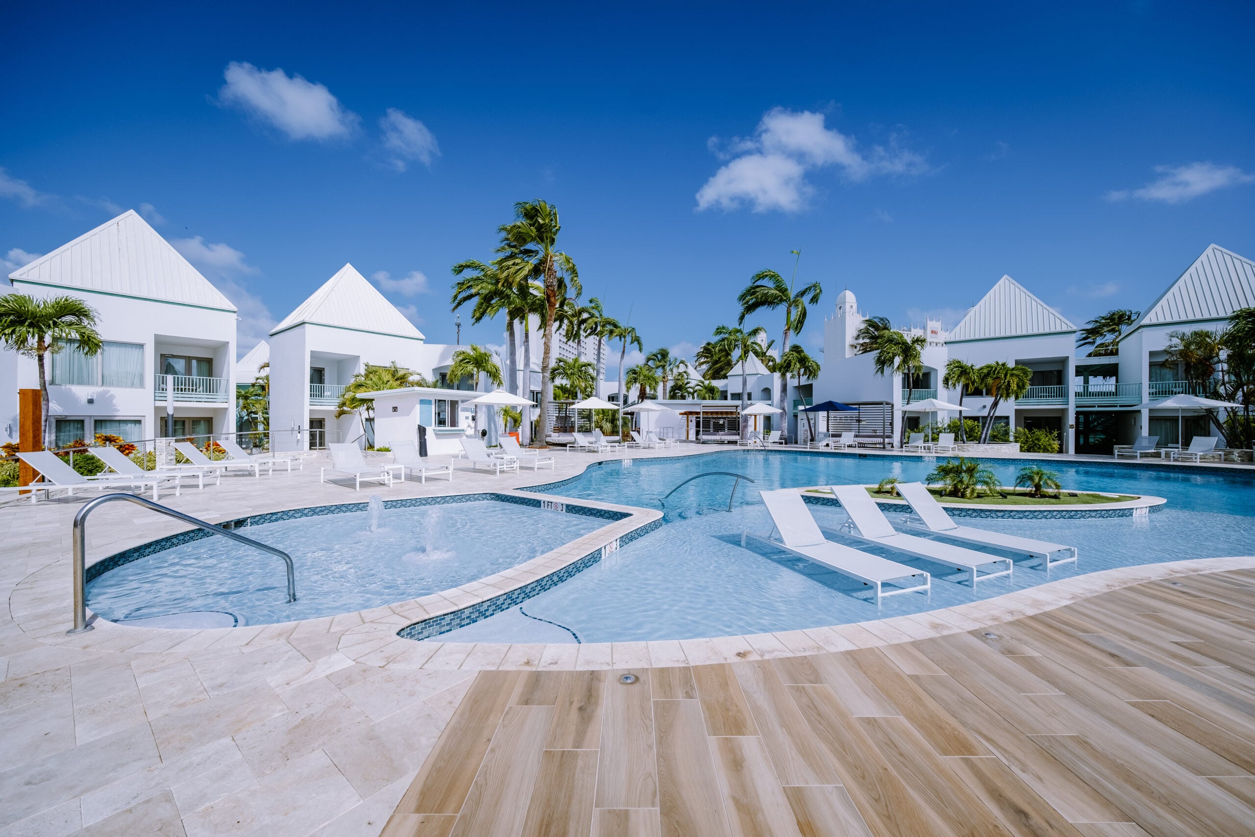 Modern swimming pool area with lounge chairs, surrounded by palm trees and white buildings, emphasizing aquatic facility maintenance and safety.