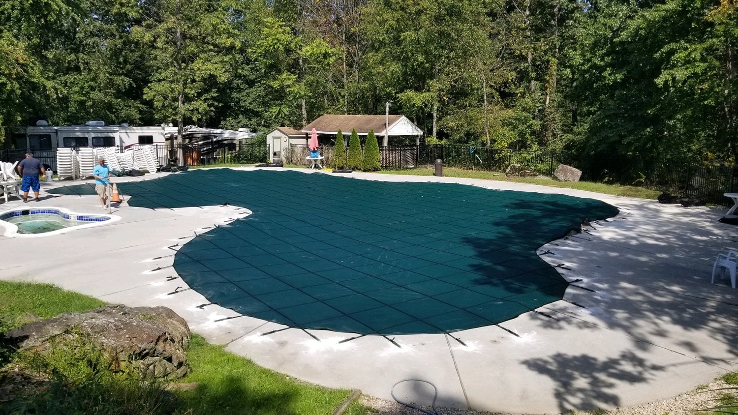 Pool covered with a green safety cover during winterization, with workers preparing the area, emphasizing pool maintenance and protection services.