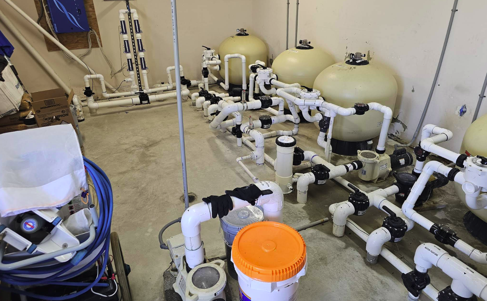 Commercial pool filtration system featuring multiple large sand filters, interconnected PVC piping, and a pump, illustrating advanced aquatic solutions for facility maintenance.
