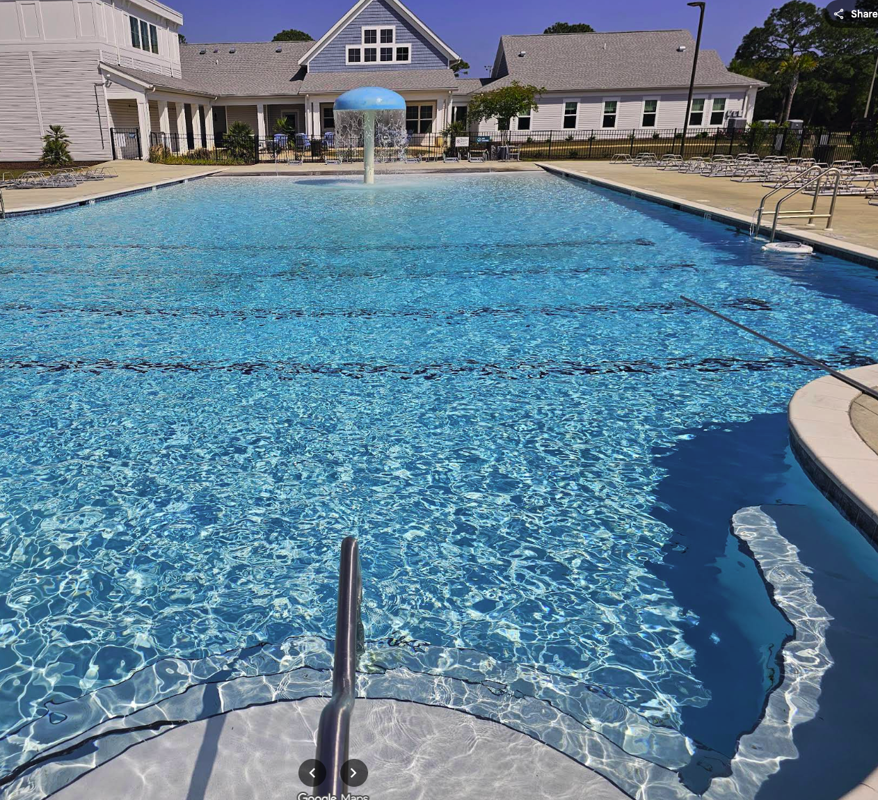 Multi-family property pool with clear blue water, featuring a splash pad, lounge chairs, and surrounding residential buildings, illustrating maintenance challenges and solutions in aquatic facility management.