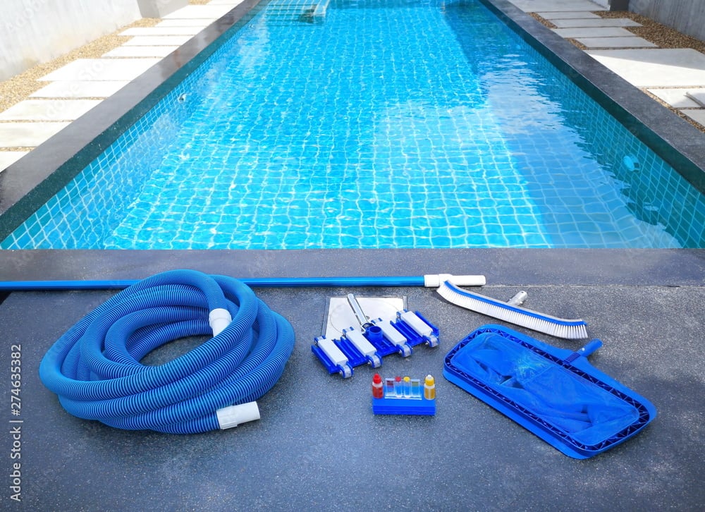 Pool cleaning equipment including hoses, brushes, and testing kits beside a clear blue swimming pool, highlighting maintenance tools for aquatics services.