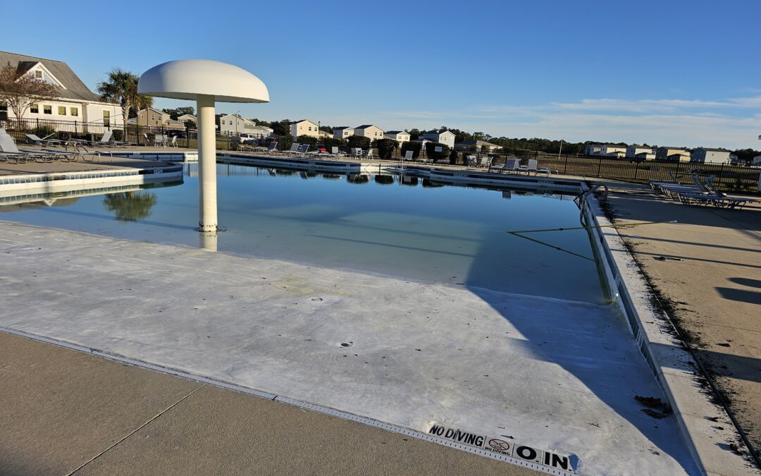 Commercial pool at military housing facility with water reflecting the sky, featuring a mushroom fountain and poolside lounge chairs, emphasizing pool compliance and renovation standards.