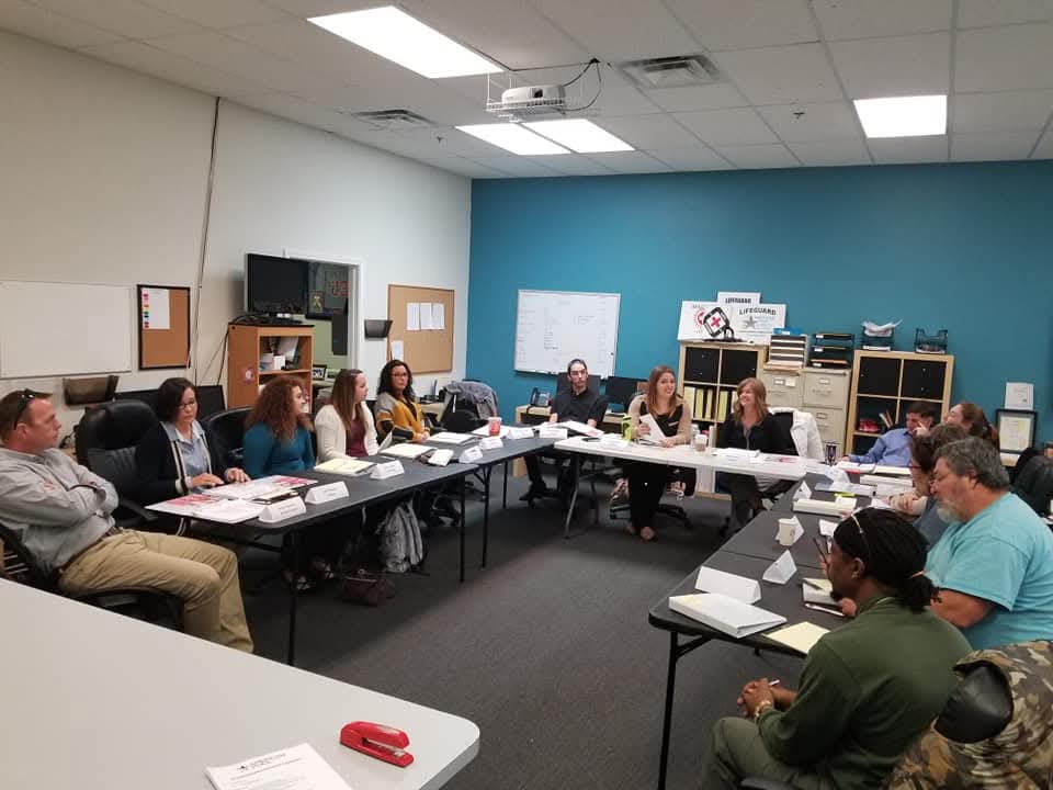 Group of professionals engaged in a pool safety and compliance workshop, seated around a conference table with documents and materials, in a well-lit meeting room.