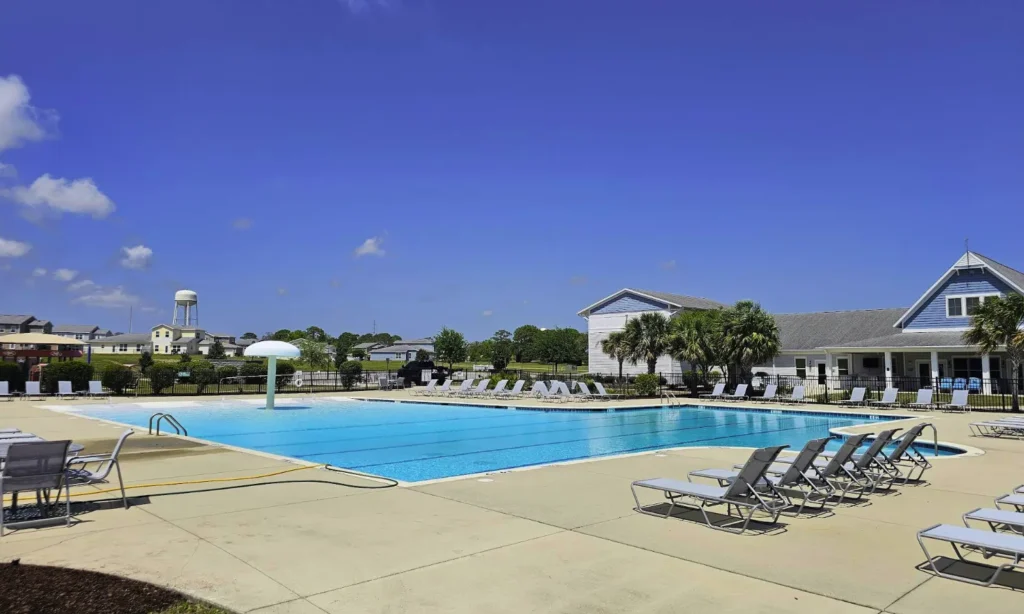 Outdoor swimming pool surrounded by lounge chairs and a clubhouse.